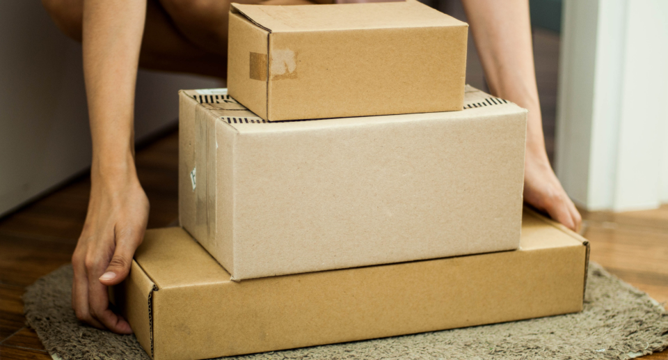 amazon boxes, woman crouching down holding three brown boxes from online shopping, amazon canada coupon hacks online shopping
