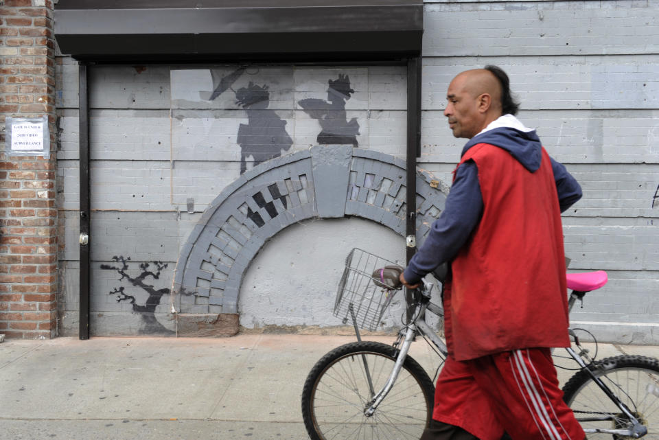 A man walks by work of British graffiti artist Banksy on Saturday, Oct. 19, 2013, in the Brooklyn borough of New York. The building owner has hired security guards and installed a metal gate to protect a work by Banksy. Cara Tabachnick, whose family owns the building, said the goal is to preserve the artwork "so it can be viewed and enjoyed." Most of the Banksy works that have gone up have been tagged over by others, and some have been completely erased. Mayor Michael Bloomberg said last week that graffiti ruins property and is "a sign of decay." (AP Photo/Alyssa Goodman)