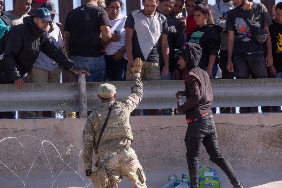 A Texas National Guard soldier tells migrants to retreat towards the border wall as they try to get water from a fellow migrant at the border between Ciudad Juarez and El Paso,