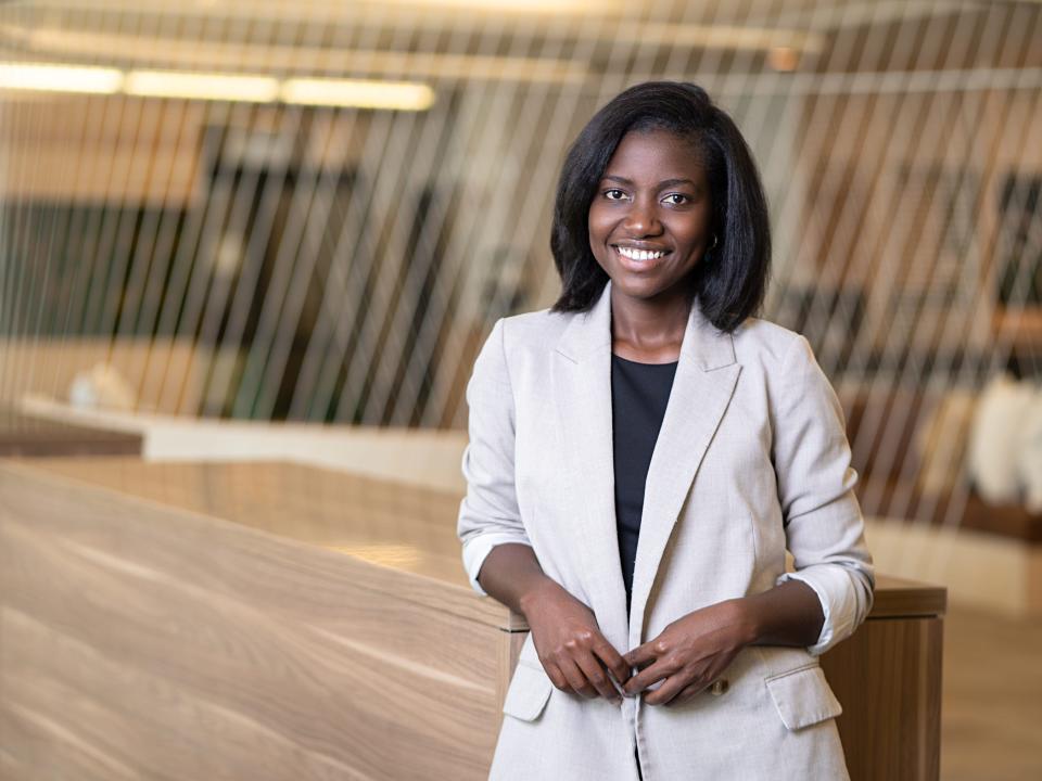 A woman stands wearing a suit, smiling to the camera