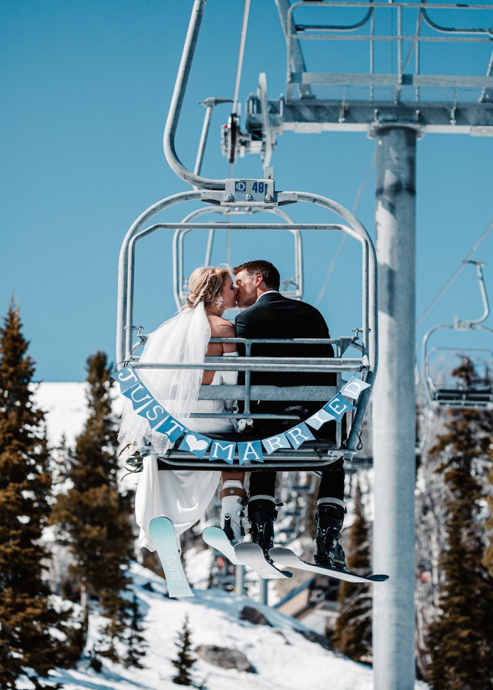 A bride and groom kiss on a ski lift with a "just married" banner attached to it.