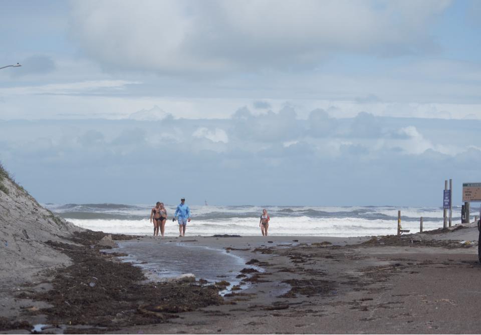 Beachgoers walk toward Access Road 6 on North Padre Island as waves and storm clouds surge along the coast.