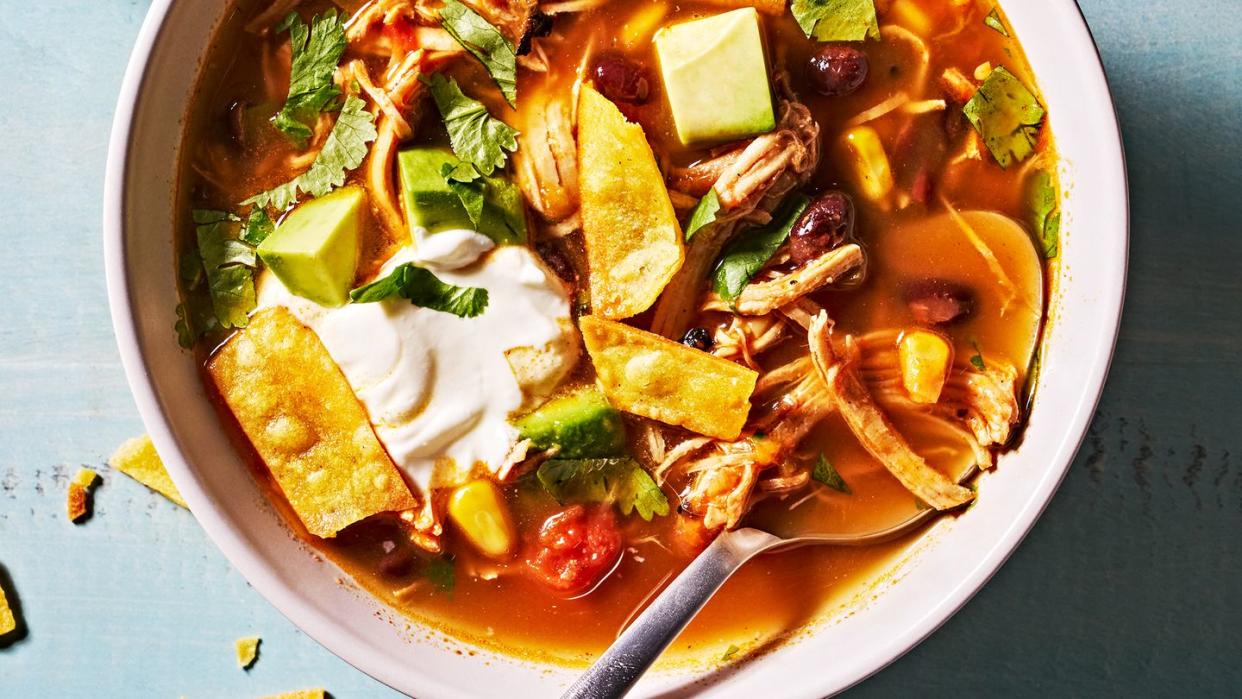 slow cooker chicken tortilla soup with sour cream, avocado slices, cheese and tortilla strips