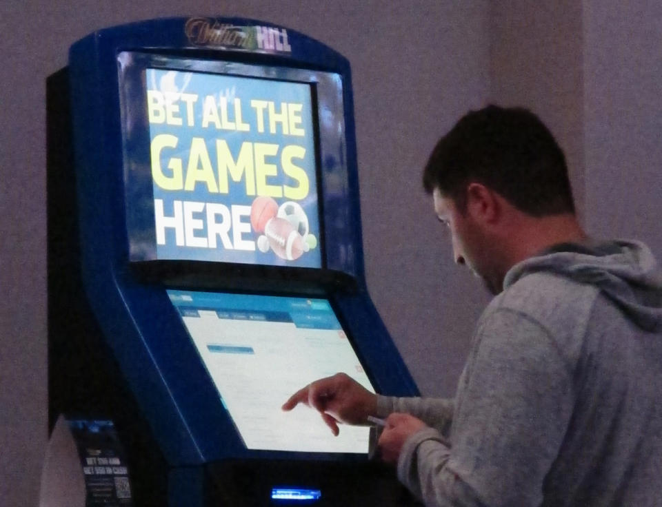 This June 21, 2019 photo shows a gambler making bets at a William Hill kiosk inside the Ocean Casino Resort in Atlantic City, N.J. On Monday, June 24, William Hill announced it is donating $50,000 it received from a lawsuit accusing rival FanDuel of copying its betting guide to a New Jersey college to fund creative writing classes. (AP Photo/Wayne Parry)
