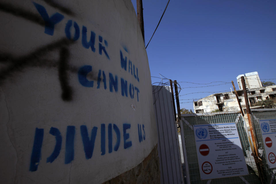 In this photo taken on Wednesday Nov. 6, 2019, graffiti on a wall reading "Your wall can not divide us" is seen at the U.N buffer zone by a fence that divides the Greek Cypriot south and the Turkish Cypriot north, in divided capital Nicosia, Cyprus. As the world commemorates 30 years since the fall of the Berlin Wall, the bullet-riddled sandstone walls of abandoned, crumbling homes and concrete machine gun nests dotting in Cyprus' no-man's land are a reminder of Europe's last divided country. (AP Photo/Petros Karadjias)