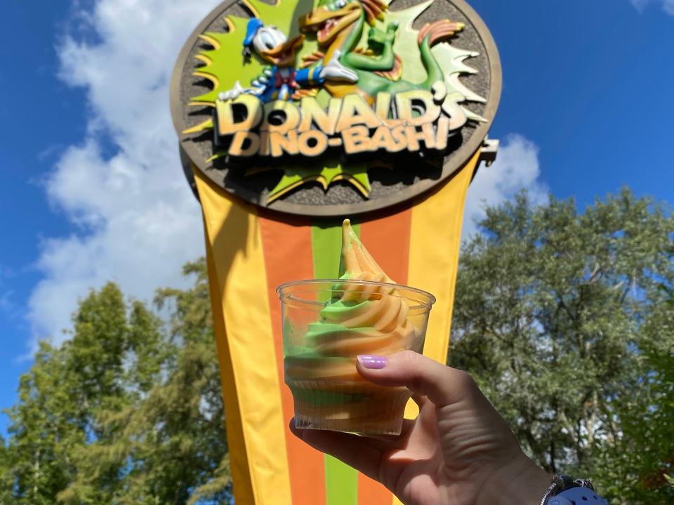 hand holding cup of green and orange soft serve at disney animal kingdom