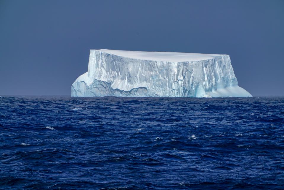 A blue-tinged iceberg, it's backside worn smooth by the waves, floats in the waters off Antarctica.