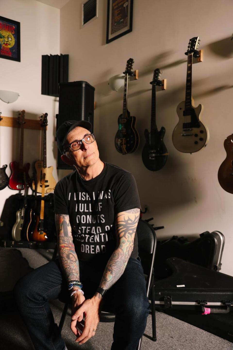 Man sitting in a studio in front of a wall of guitars