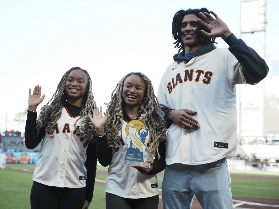 This photo provided by the CalHope Courage Award shows Twins Amaya and Anysa Gray, and Nigel Wilson wave after being presented with the CalHope Courage Award before a baseball game between the San Francisco Giants and Washington Nationals on Tuesday, May 9, 2023, at Oracle Park in San Francisco. (Daniel Moebus-Bowles/CalHope Courage Award via AP)
