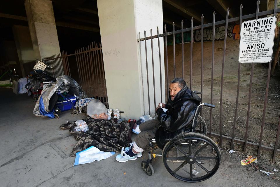 An unhoused man sits in his wheelchair beside a sign warning against camping, loitering and littering at a homeless encampment beneath a freeway overpass near SoFi Stadium, where the Superbowl will be played, in Inglewood, California, which is adjacent to the city of Los Angeles and a part of L.A. County.