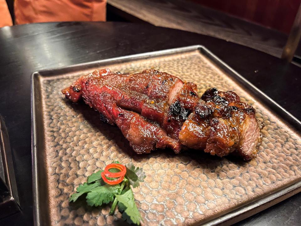 A piece of brown, crispy looking pork on a square metal tray with an herb sprig next to the meat