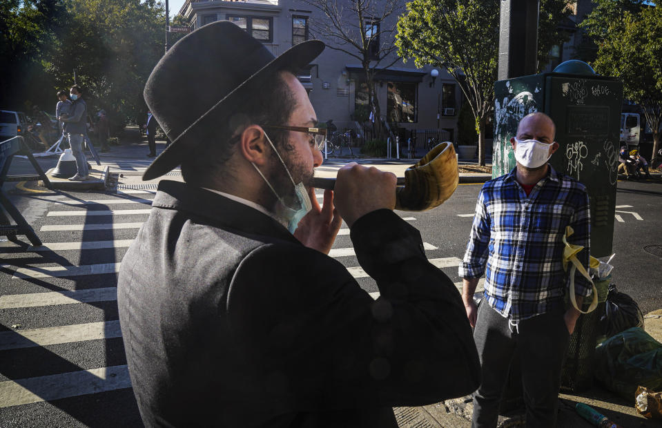 FILE - In this Sept. 20, 2020, file photo, an Orthodox Jewish man blows the Shofar after a brief prayer with a passerby in New York. Amid a new surge of COVID-19 in New York’s Orthodox Jewish communities, many residents are reviving health measures that some had abandoned over the summer – social distancing, wearing masks. For many, there’s also a return of anger: They feel the city is singling them out for criticism that other groups avoid. (AP Photo/Bebeto Matthews, File)