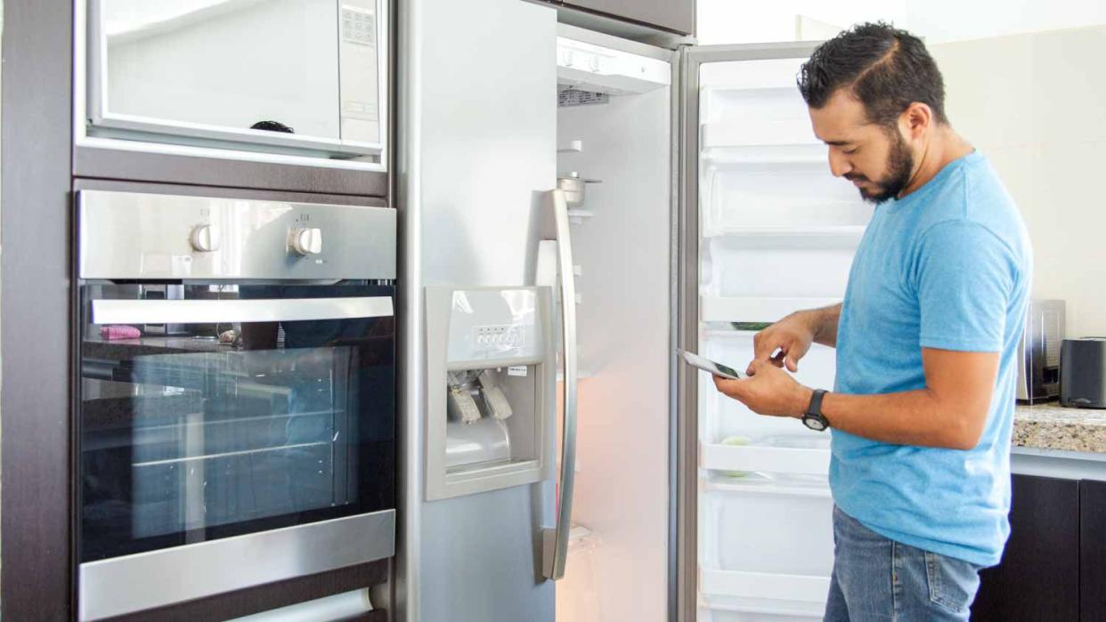 Man checking his phone in front of a refrigerator