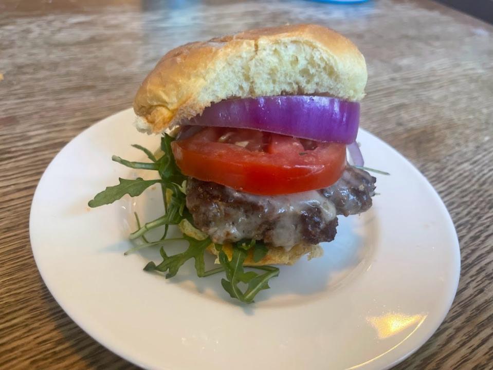 A slider with arugula, a slice of tomato, and a red-onion slice sit between hamburger buns