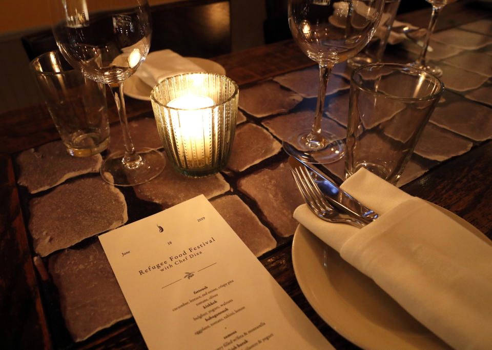 In this June 18, 2019, photo, a special menu for the Refugee Food Festival sits on a candle-lit table at Porsena, an Italian restaurant in Manhattan's East Village, to inform diners of the Mediterranean specialties that will be served for just one night, in New York. The annual global festival promotes refugee chefs like Syrian refugee Diaa Alhanoun, noted as "Chef Diaa," on the menu. It is the second consecutive year Alhanoun has prepared a meal for Porsena's patrons. (AP Photo/Kathy Willens)