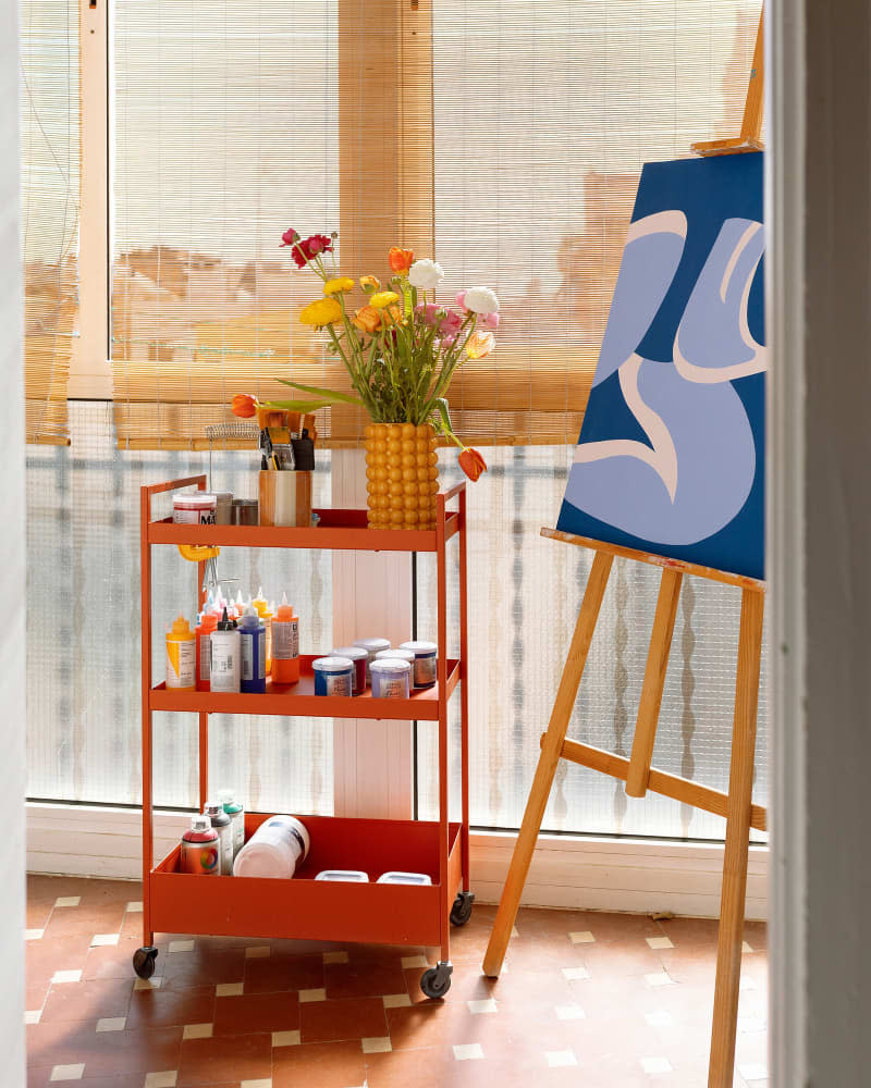 An orange cart with art supplies next to the artwork on an easel.