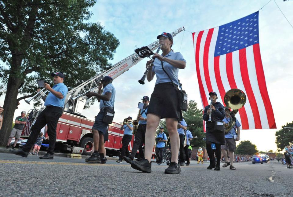 A band marches beneath a giant American flag draped by Quincy Fire Department ladder trucks during the Quincy Flag Day Parade, Saturday, June 11, 2022.