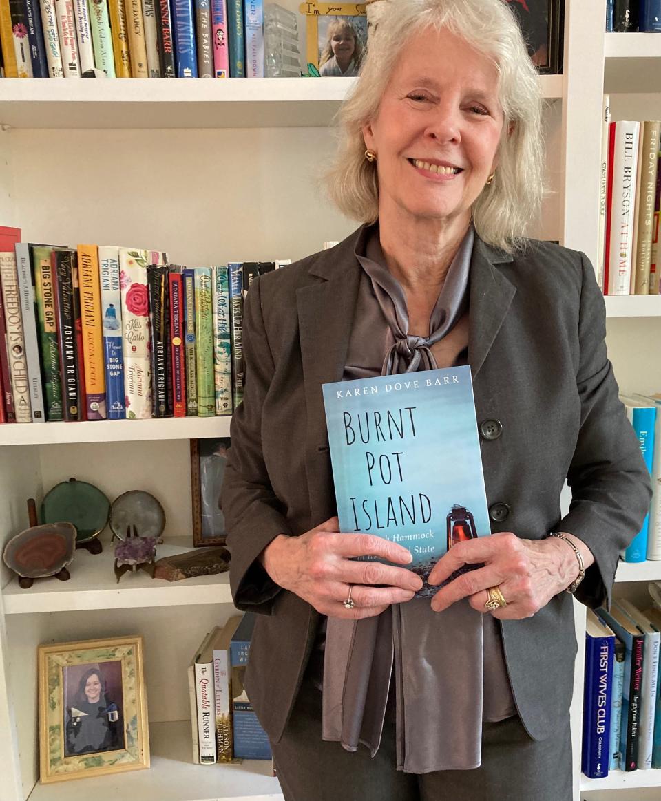 Author Karen Dove Barr at home with books, holding her first novel "Burnt Pot Island"