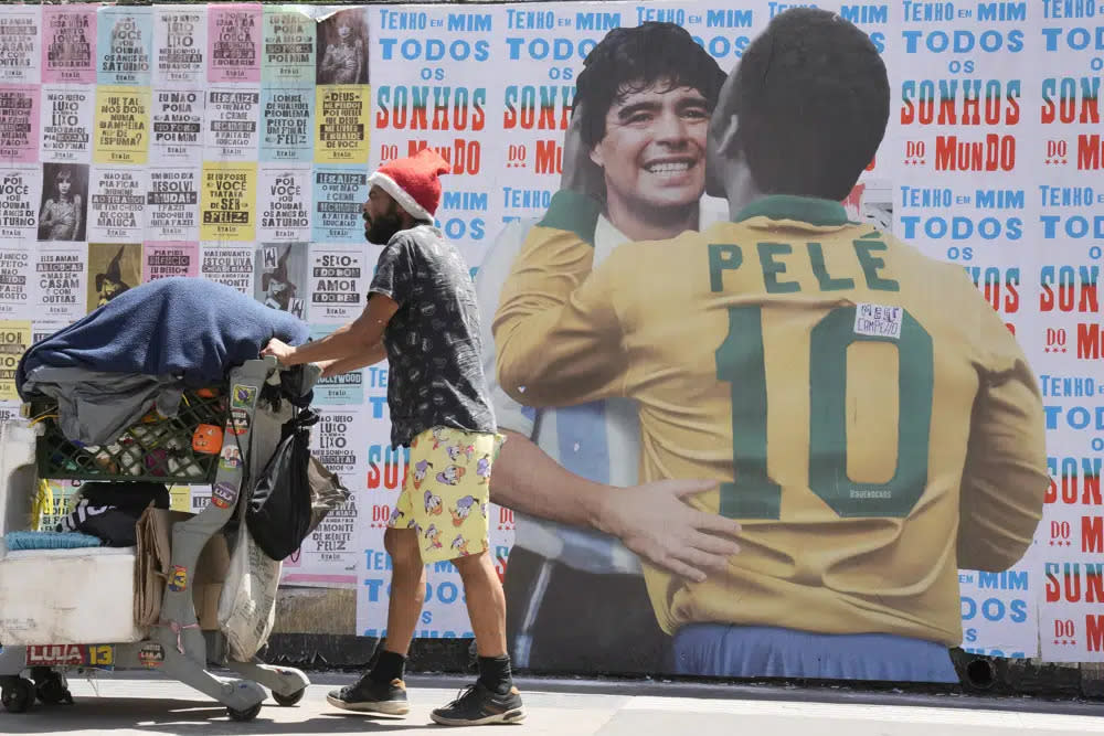 A man pushes a cart loaded with garbage for recycling in front of a mural depicting Brazilian soccer legend Pele embracing late Argentinean soccer star Diego Maradona in Sao Paulo, Brazil, Saturday, Dec. 24, 2022. (AP Photo/Andre Penner)