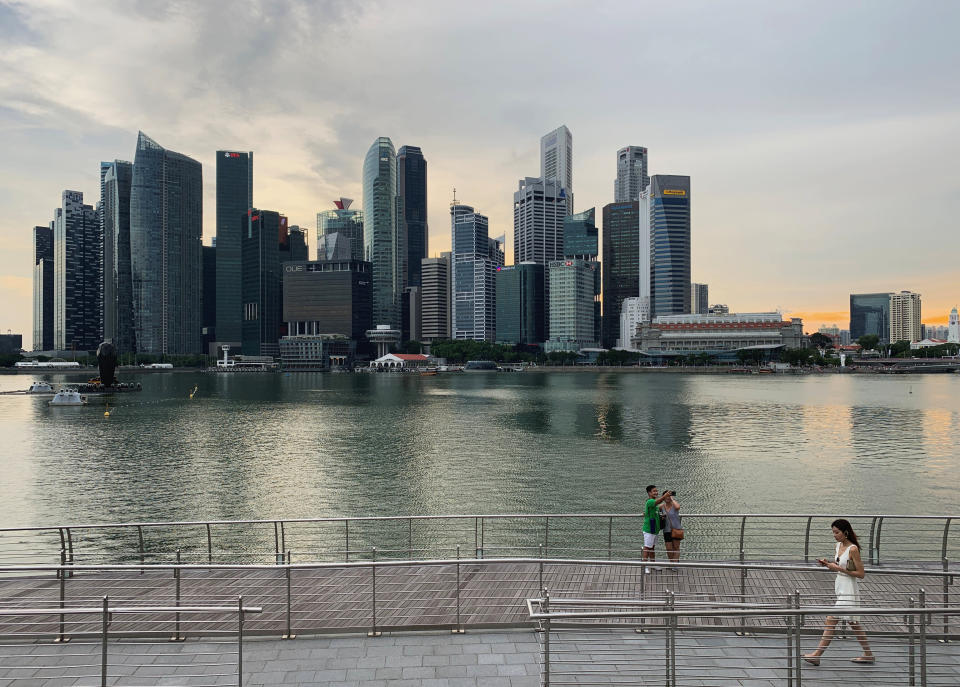 A passer-by looks at her mobile phone as people take a selfie photo using a smartphone, with Singapore's central business district skyline, in Singapore, May 10, 2019. REUTERS/Kevin Lam