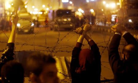 Anti-Mubarak protesters gesture after former Egyptian President Hosni Mubarak's verdict, in front of barbed wire, soldiers with armoured personnel carriers (APCs) and police vehicles as they close one of the entrances which lead to Tahrir square in downtown Cairo November 29, 2014. REUTERS/Amr Abdallah Dalsh