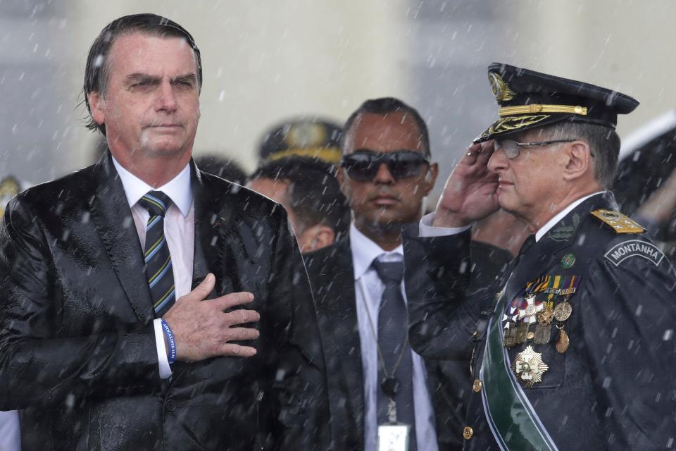 FILE - In this April 17, 2019 file photo, Brazil's President Jair Bolsonaro puts his hand over his heart as Army Commander Edson Leal Pujol salutes during the playing of the national anthem during a ceremony under the pouring rain to mark Army Day in Brasilia, Brazil. Heading into his second year as president, Bolsonaro has held firm to his combative culture-warrior policies while feuding with critics at home and abroad. (AP Photo/Eraldo Peres, File)