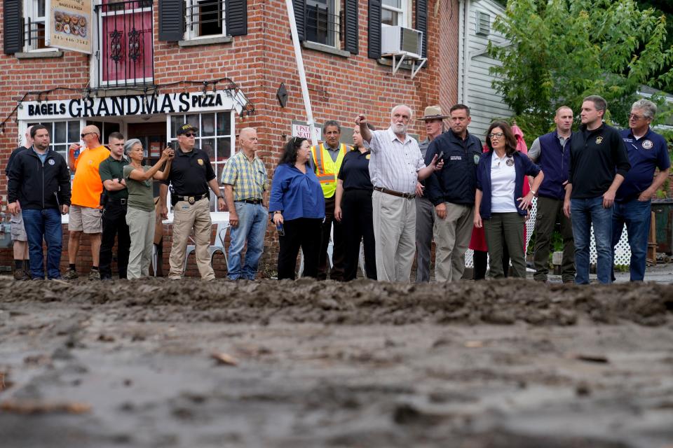 Governor Kathy Hochul, fourth from right, and an entourage of emergency workers, resident, and journalists pass along Main Street damaged the previous day by floodwaters, Monday, July 10, 2023, in Highland Falls, N.Y. Heavy rain has washed out roads and forced evacuations in the Northeast as more downpours were forecast throughout the day. One person in New York's Hudson Valley has drowned as she was trying to leave her home. (AP Photo/John Minchillo)