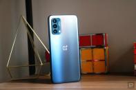 <p>OnePlus Nord N200 5G. Off angle view of the phone sitting on a shelf with ornaments in the background with its rear facing outwards.</p> 