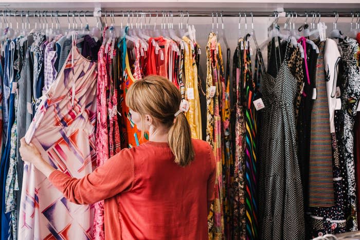A woman stands with her back to the camera, browsing a rack of dresses in various patterns and styles