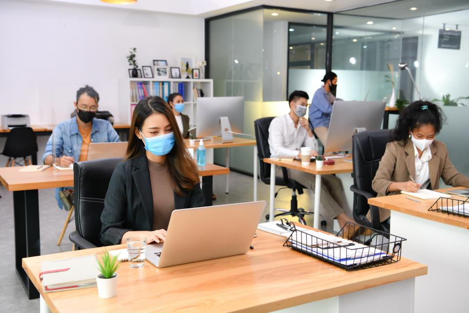 Asian office workers wearing face masks working in the new normal office and doing social distancing during coronavirus covid-19 pandemic