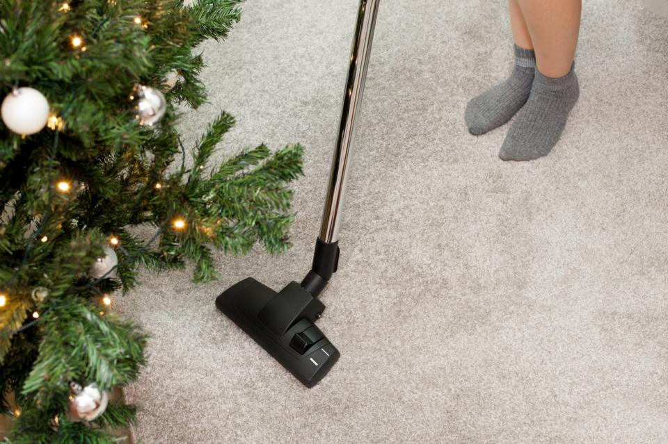 Person using a stick vacuum to clean the carpet near a Christmas tree.