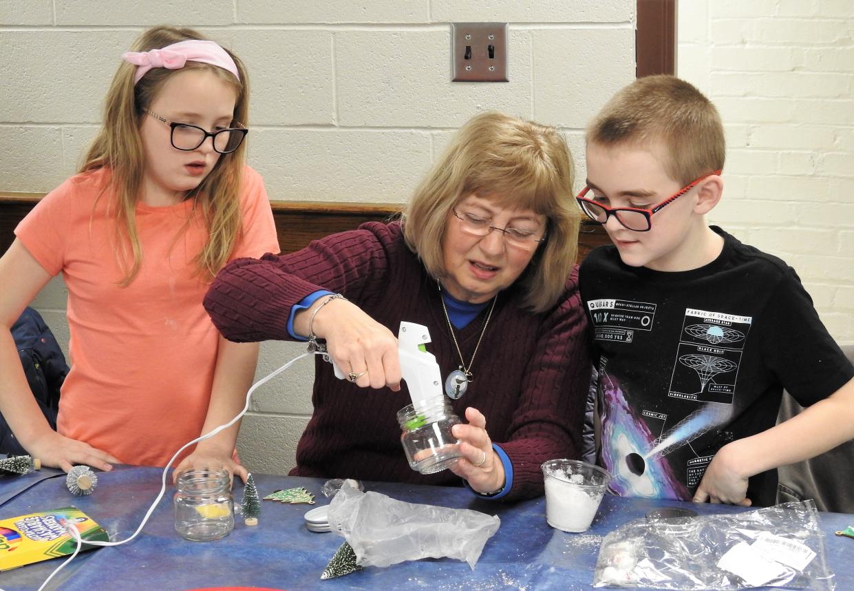 Julie Brode uses a hot glue gun to assist her grandchildren Jase Haines and Addison Haines, both 8. Youth Services Coordinator Laiken Bantum led a snow globe craft at Coshocton Public Library. About 15 youth were registered. Kids used snowmen, animal and tree figurines and fake snow to create do-it-yourself snow globes in glass jars to take home.