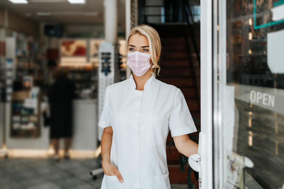 female pharmacist with face protective mask standing at open drugstore