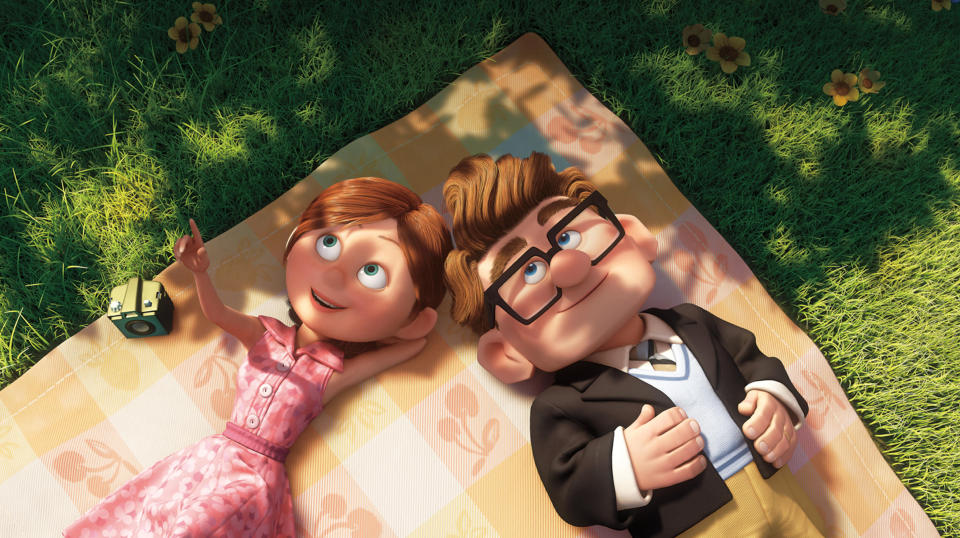 Ellie and Carl from the animated movie "Up" lie on a picnic blanket on the grass, looking up at the sky. Ellie points upward while Carl holds his hands on his chest