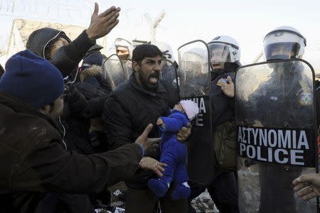 A stranded migrant holding a baby shouts next to a Greek police cordon following scuffles at the Greek-Macedonian border, near the village of Idomeni, Greece, December 3, 2015. REUTERS/Alexandros Avramidis