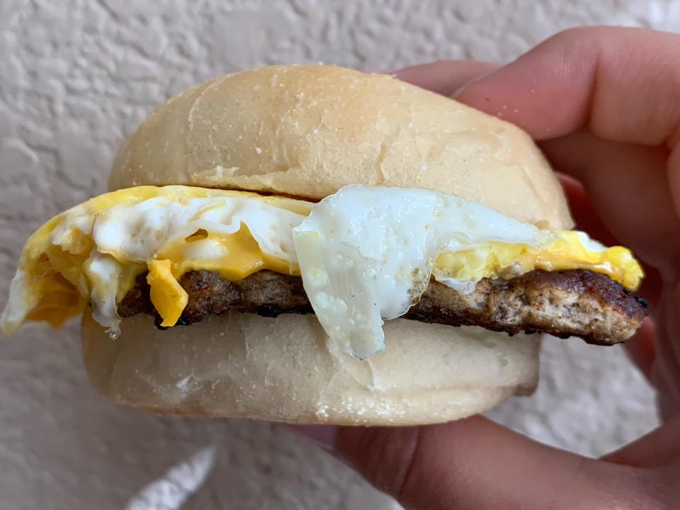 Hand holding Wendy's classic sausage, egg, and cheese sandwich in front of white wall