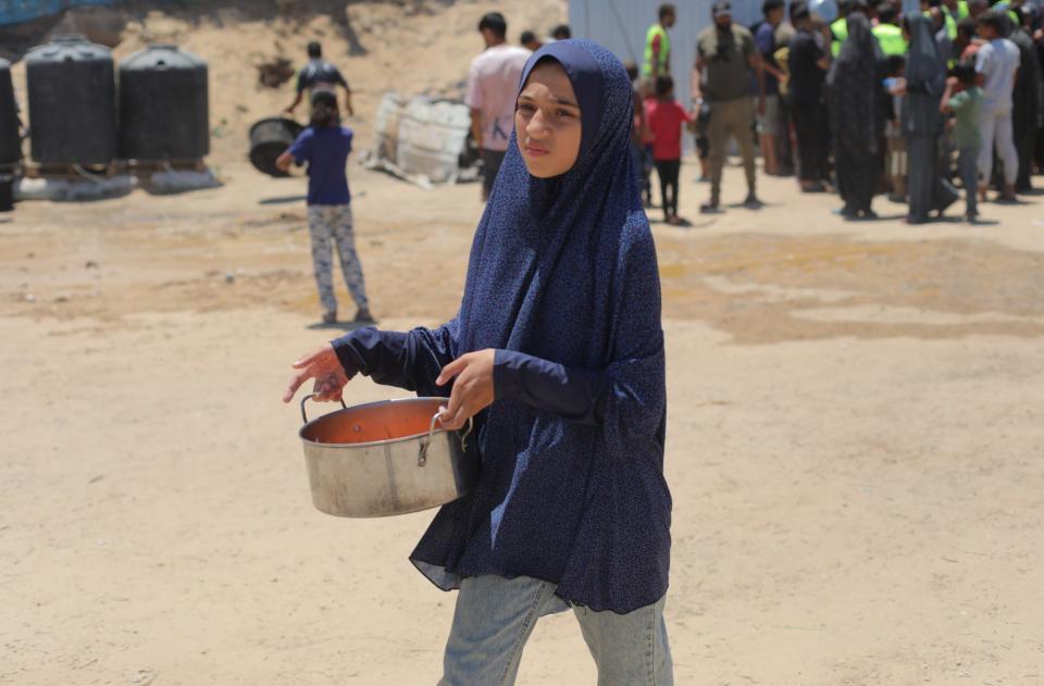 A Palestinian child carries container full of food as Palestinians, including children, wait in line to receive food distributed by charitable organizations amidst Israeli attacks in Deir Al- Balah, Gaza