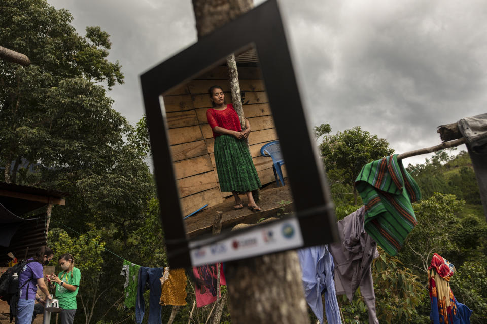 Irma Cal Pop, 26, is reflected in a mirror donated by USAID while members of the CrossPoint Baptist Church of Alabama, help to install an energy saving kitchen in her home, in the makeshift settlement Nuevo Queja, Guatemala, Monday, July 12, 2021. Mirrors donated by USAID hang inside every ramshackle home of the makeshift settlement. (AP Photo/Rodrigo Abd)