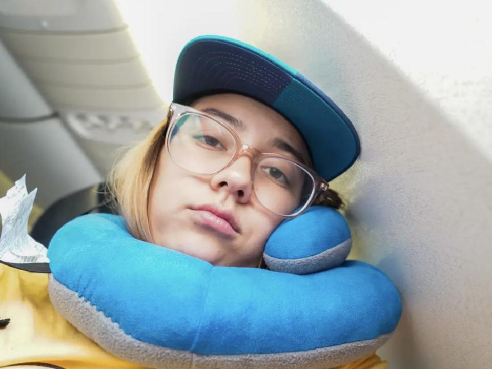 The author leans agains a plane wall with a blue neck pillow on