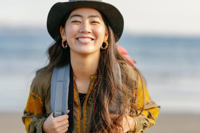 Someone is outdoors in a hat, smiling broadly. 