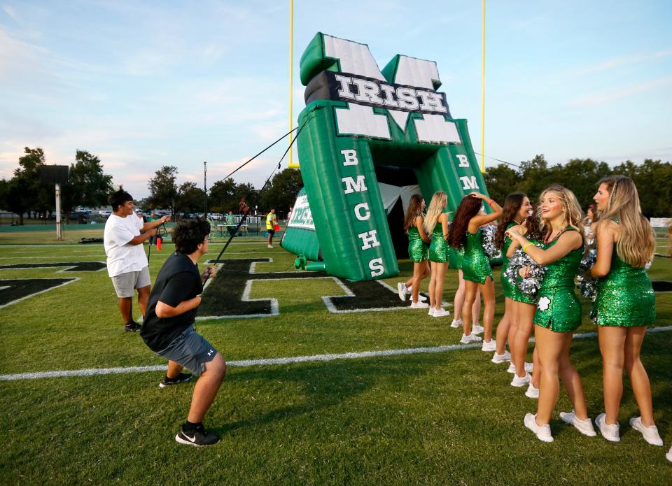 Bishop McGuinness students try to keep the team’s inflatable tunnel from blowing away as the pom squad waits for the team to take the field before a game in 2021.