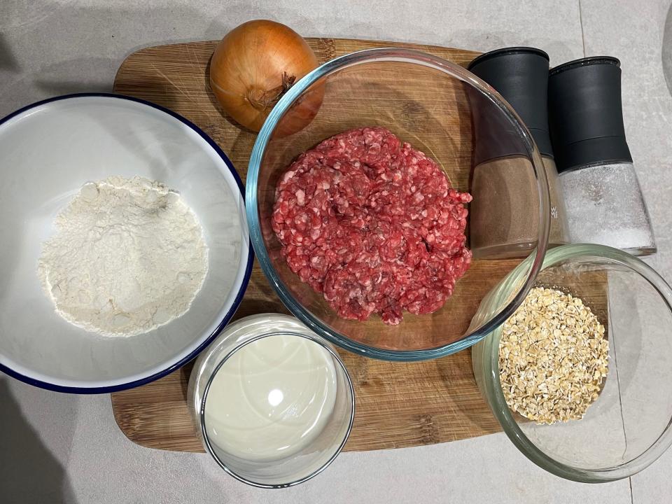 flour, ground meat, oats, an onion, and spices for ree drummond's meatball recipe on a wooden cutting board