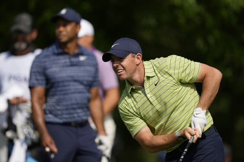 Rory McIlroy, of North Ireland, watches his tee shot as Tiger Woods looks on, on the 17th hole.