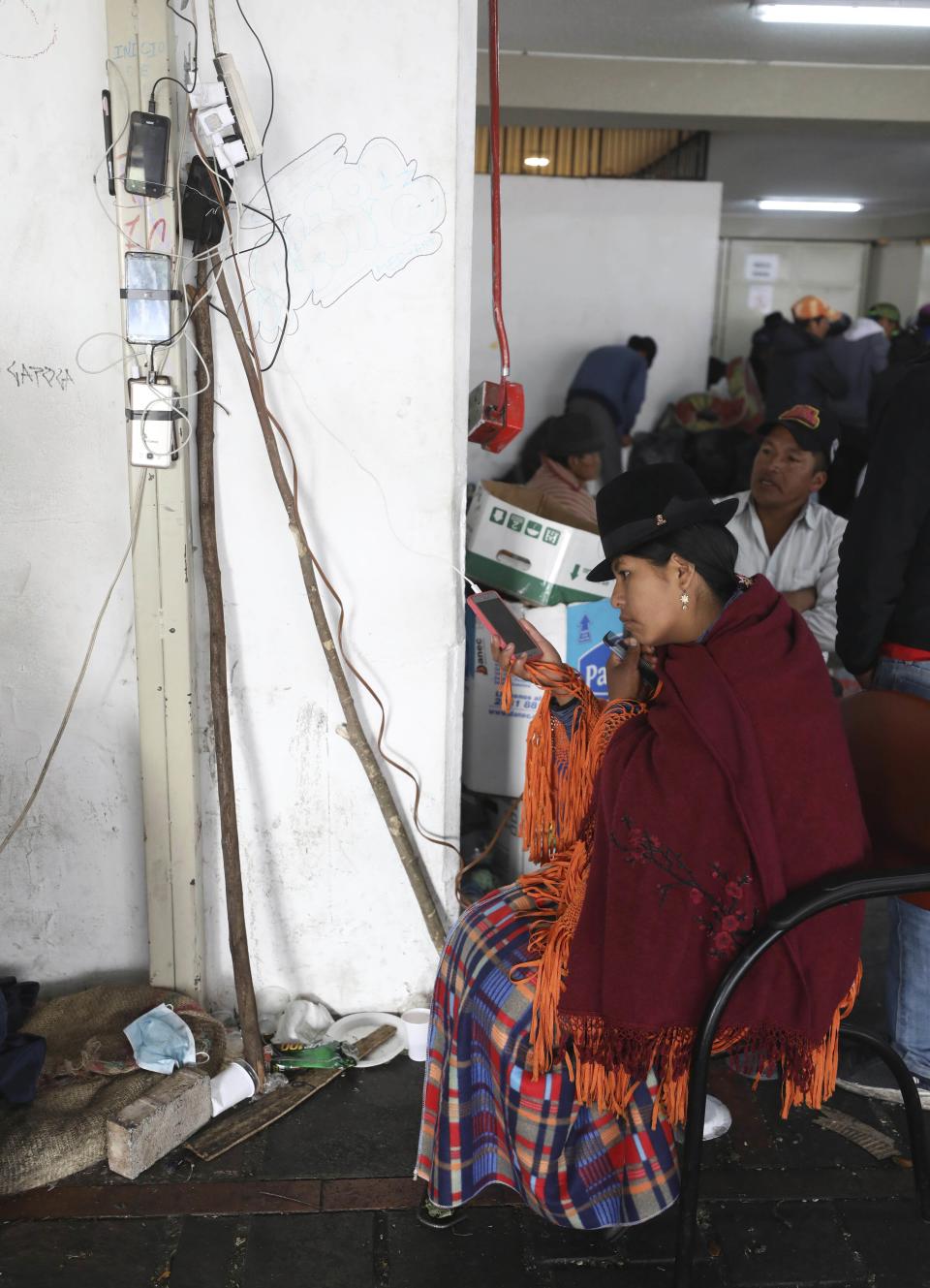 An indigenous woman, part of the many groups of people demonstrating against the government, charges her mobile phone at La Casa de la Cultura in Quito, Ecuador, Thursday, Oct. 10, 2019. Protests started last week after Ecuador's President Lenin Moreno ended fuel subsidies, leading to price increases. The disturbances have spread from transport workers to students and then to indigenous demonstrators. (AP Photo/Fernando Vergara)