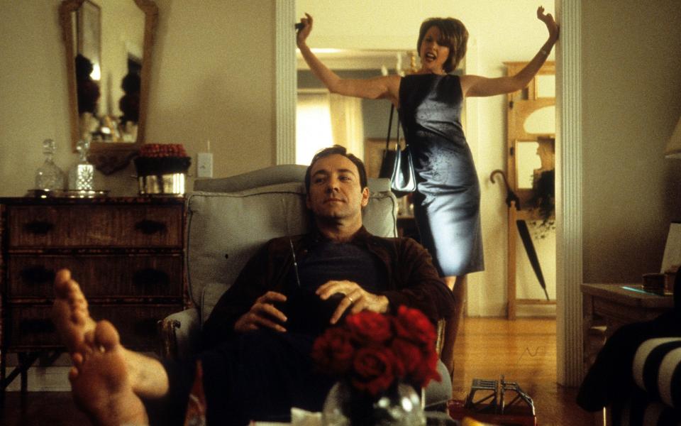 Kevin Spacey lounging in a reclining chair as Annette Bening stands in the entryway perturbed in a scene from the film 'American Beauty', 1999