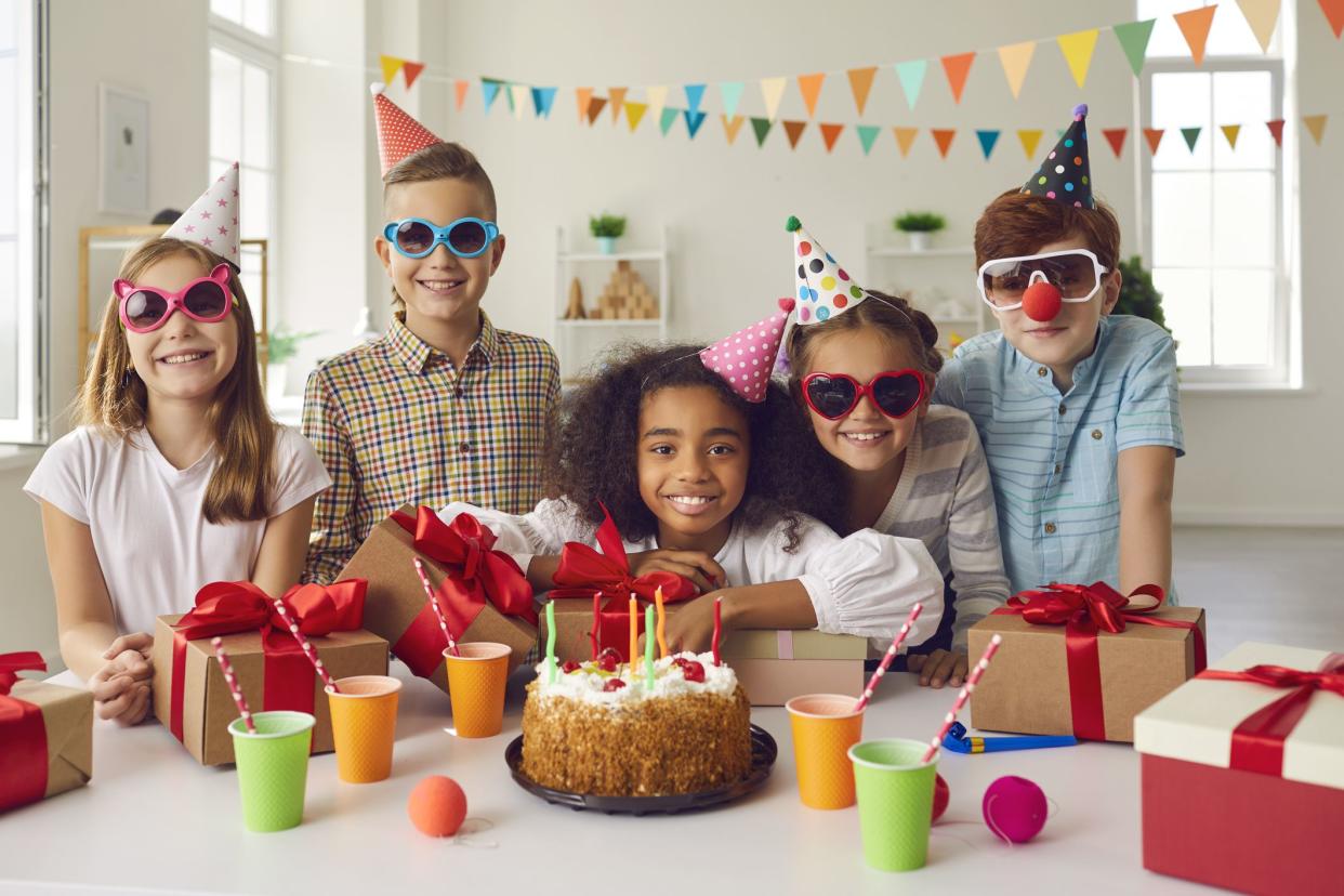 Portrait of an afro american birthday girl with her friends who are at the table with presents and a holiday cake with candles. Friends in holiday accessories have fun in a festively decorated room.