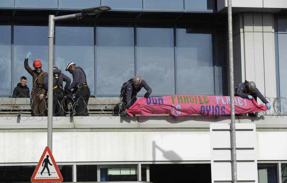Police officers wearing safety equipment remove an Extinction Rebellion demonstrator, left in red helmet, and a banner after he occupied a raised area at City Airport in London, Thursday, Oct. 10, 2019. Some hundreds of climate change activists are in London during a fourth day of world protests by the Extinction Rebellion movement to demand more urgent actions to counter global warming. (AP Photo/Matt Dunham)