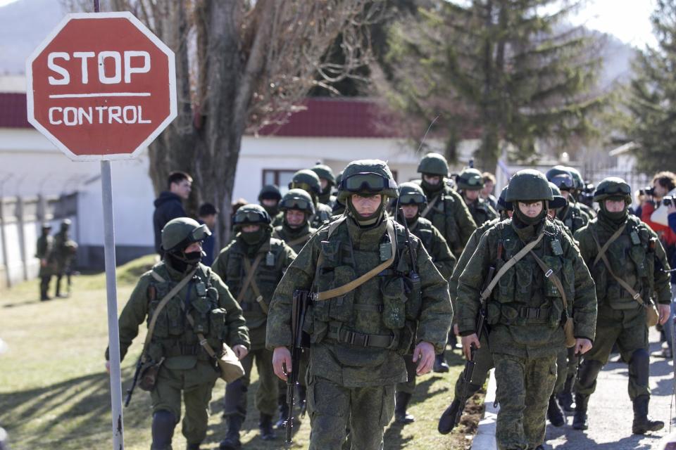 Military personnel, believed to be Russian servicemen, walk outside the territory of a Ukrainian military unit in the village of Perevalnoye outside Simferopol