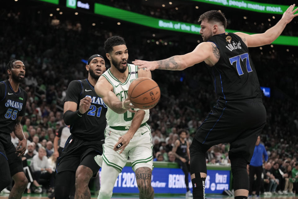 Boston Celtics forward Jayson Tatum (0) passes the ball around Dallas Mavericks guard Luka Doncic (77) as forward Derrick Jones Jr. (55) and center Daniel Gafford (21) defend during the first half of Game 1 of basketball's NBA Finals on Thursday, June 6, 2024, in Boston. (AP Photo/Charles Krupa)