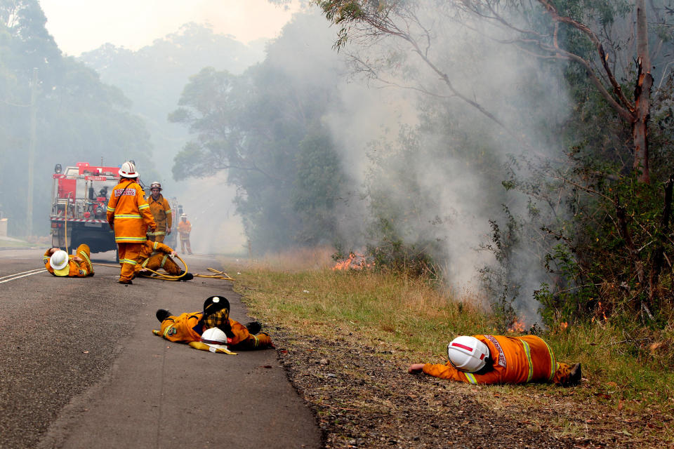 Exhausted firefighters take a rest while fire burns close by, on Crangan Bay Road, on October 18, 2013 in Nords Wharf, Australia. One man has died and hundreds of properties have been destroyed in bushfires that are devastating the Blue Mountains and Central Coast regions of New South Wales. 